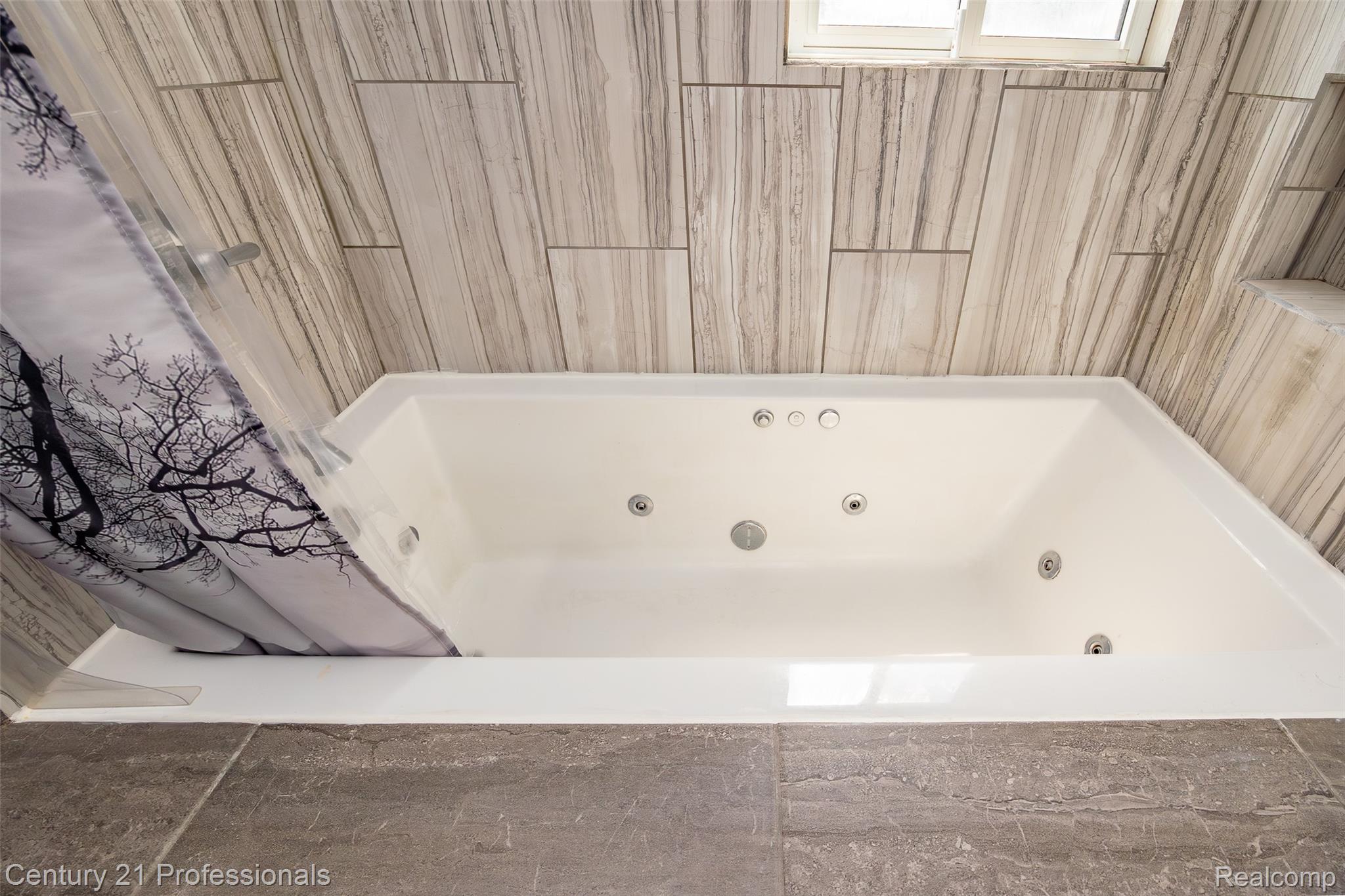 3251 Mann Road Clarkston, MI 48346 - Photo 25 of 40 White jetted bathtub with chrome fixtures, surrounded by vertically-oriented tile walls and large format tile flooring