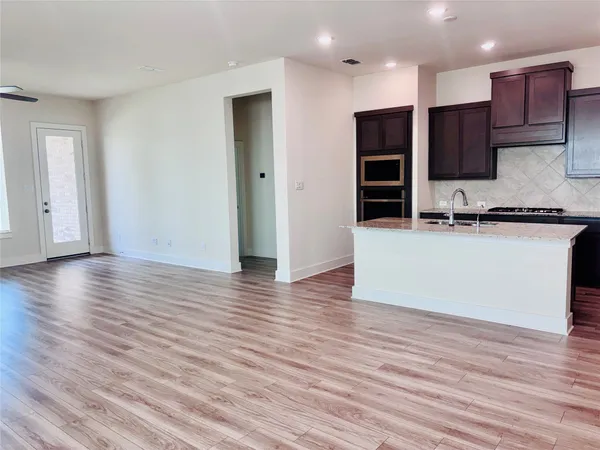 an empty room with wooden floor and a view of kitchen