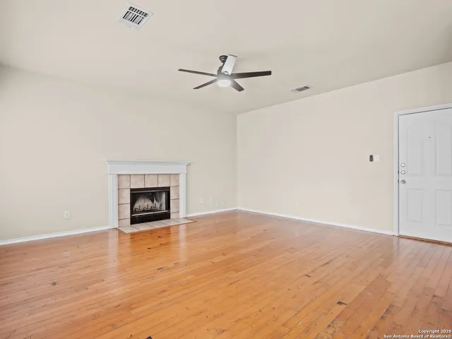 an empty room with wooden floor a ceiling fan white walls and windows