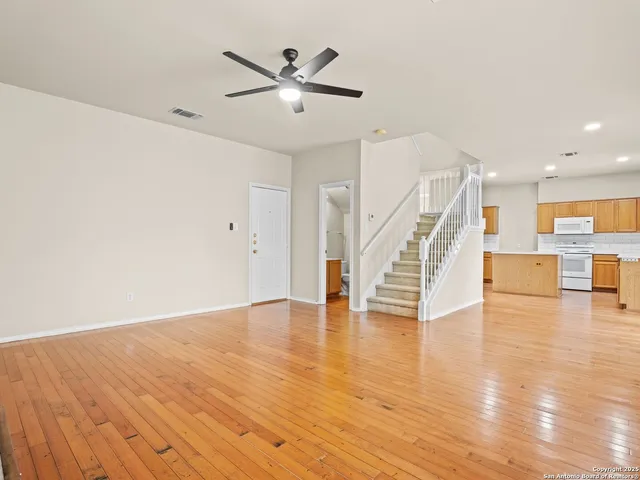 a view of an empty room with wooden floor and a ceiling fan