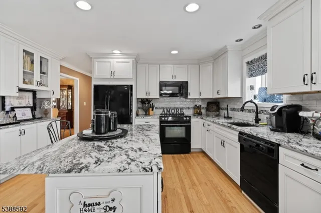 a kitchen with stainless steel appliances granite countertop a stove top oven a sink dishwasher a refrigerator and white cabinets with wooden floor