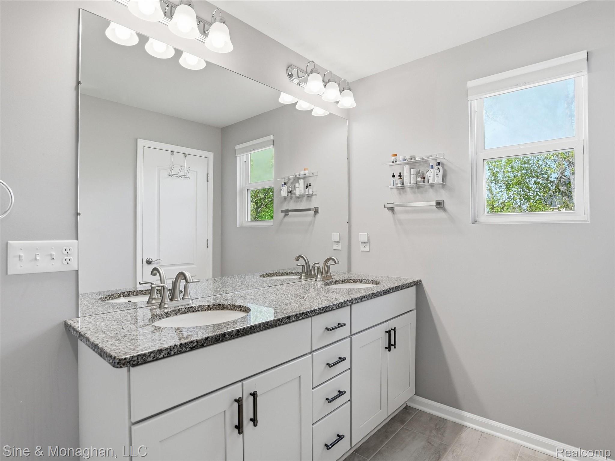 24827 Ivy Road Novi, MI 48375 - Photo 20 of 38 Double vanity featuring white shaker-style cabinetry, dark hardware, and a stone-finish countertop with undermount sinks