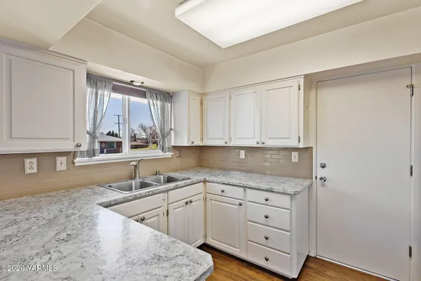 a kitchen with granite countertop a sink window and cabinets