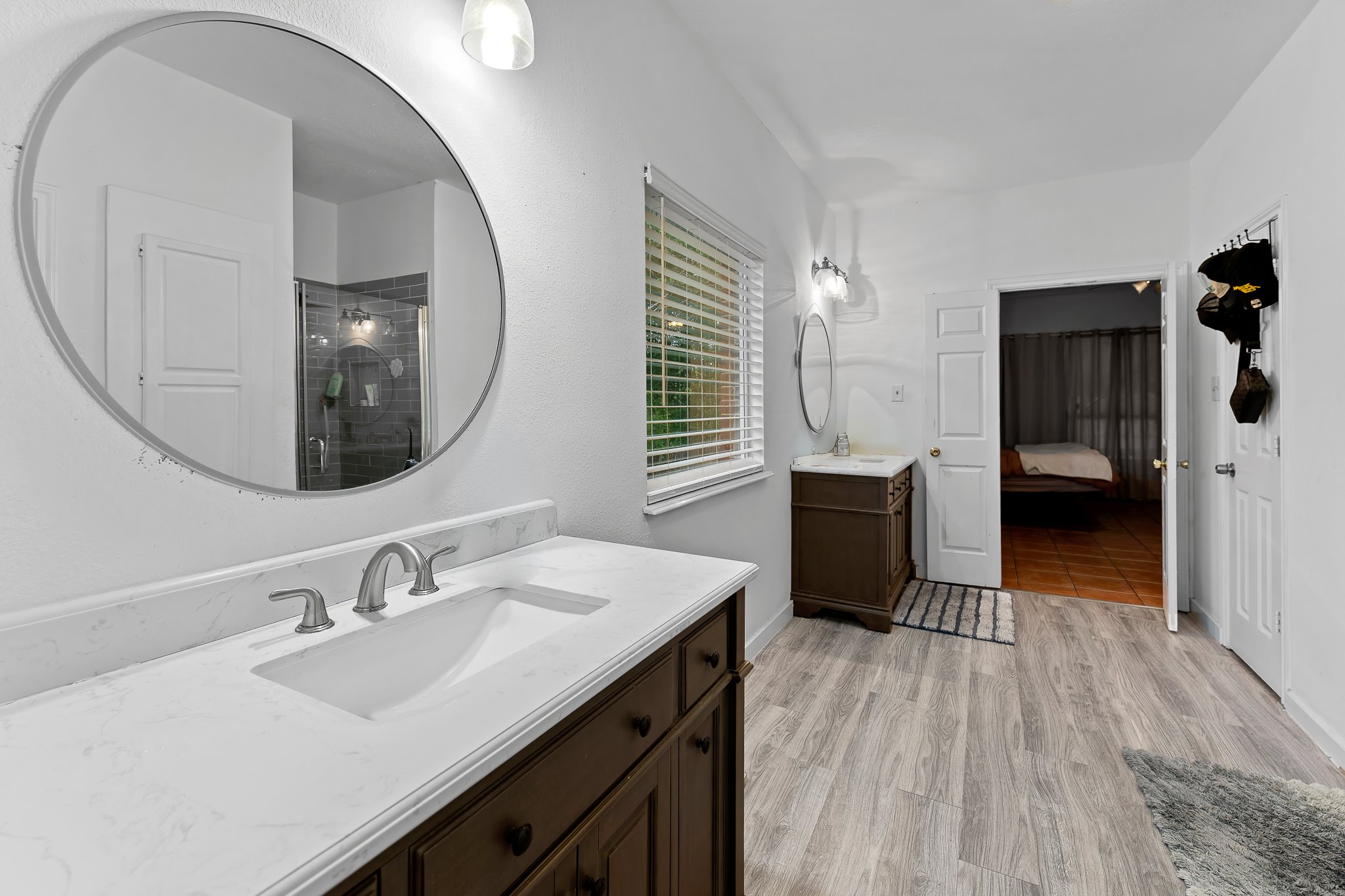 11737 Rydalwater Lane Austin, TX 78754 - Photo 21 of 40 Bathroom featuring wood-finish flooring, a white countertop vanity with an integrated sink, a large circular mirror, and a window with blinds
