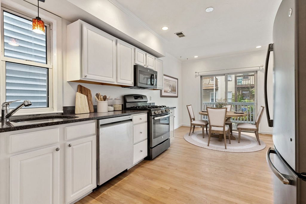 8 Peters Street, Unit B Boston, MA 02127 - Photo 2 of 14 a kitchen with stainless steel appliances granite countertop a stove top oven a sink a dining table and chairs with wooden floor