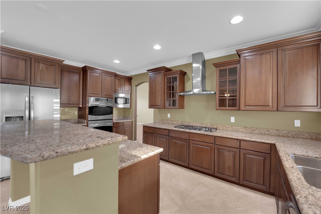 10057 Portula Valley Street Las Vegas, NV 89178 - Photo 13 of 56 Kitchen with glass insert cabinets, wall chimney range hood, recessed lighting, light stone counters, and ornamental molding