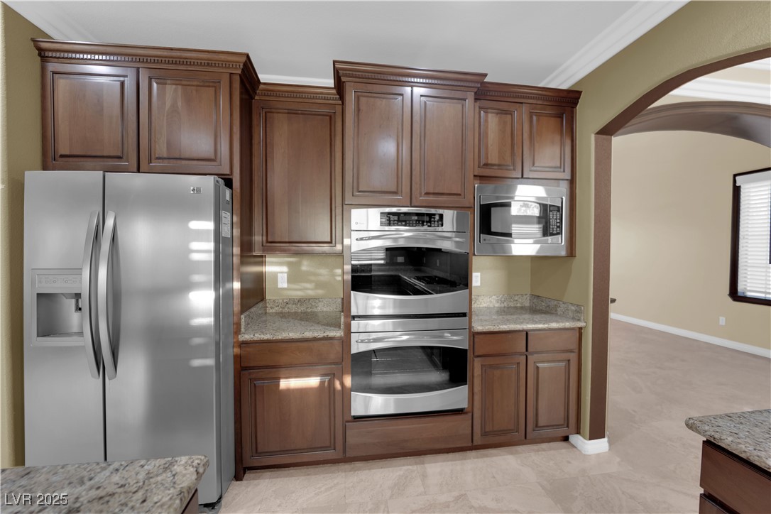 10057 Portula Valley Street Las Vegas, NV 89178 - Photo 15 of 56 Kitchen with arched walkways, stainless steel appliances, light stone counters, and ornamental molding