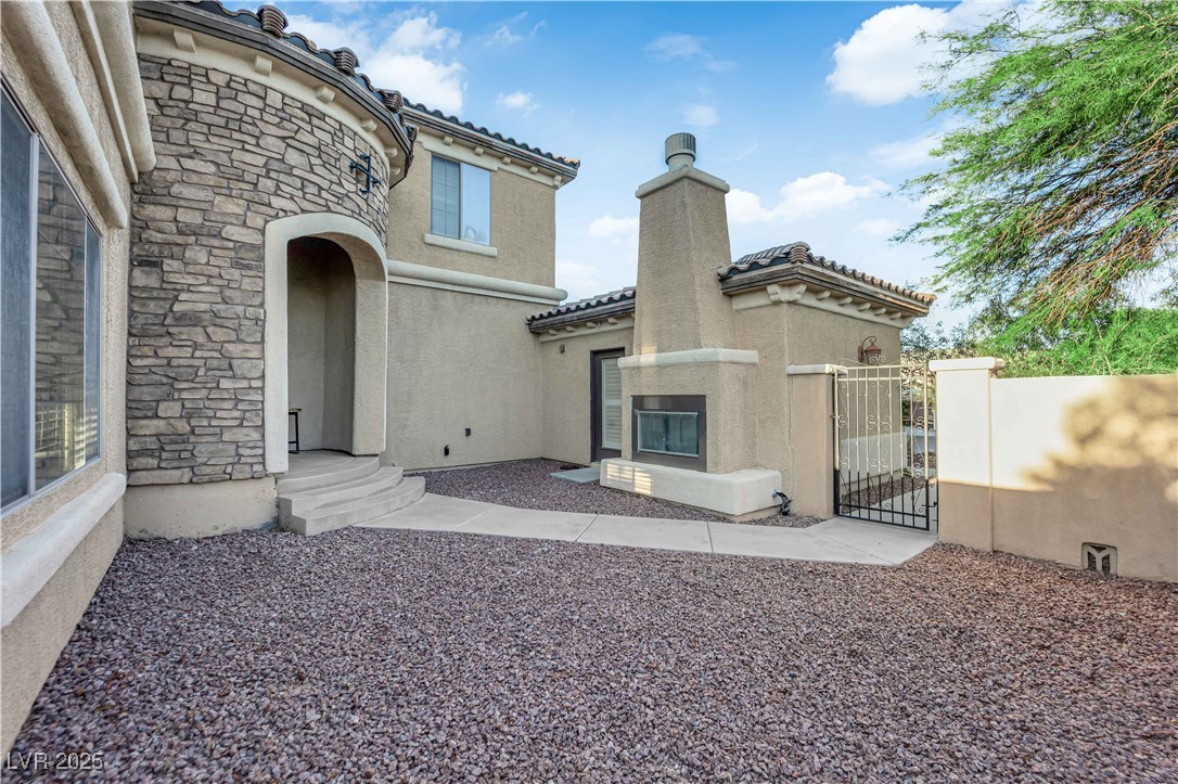 10057 Portula Valley Street Las Vegas, NV 89178 - Photo 4 of 56 Back of property featuring a gate, stone siding, stucco siding, and a tile roof