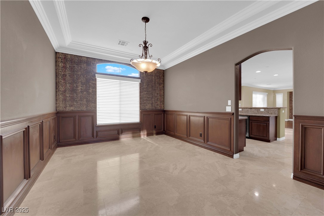 10057 Portula Valley Street Las Vegas, NV 89178 - Photo 9 of 56 Unfurnished dining area with arched walkways, ornamental molding, and a wainscoted wall
