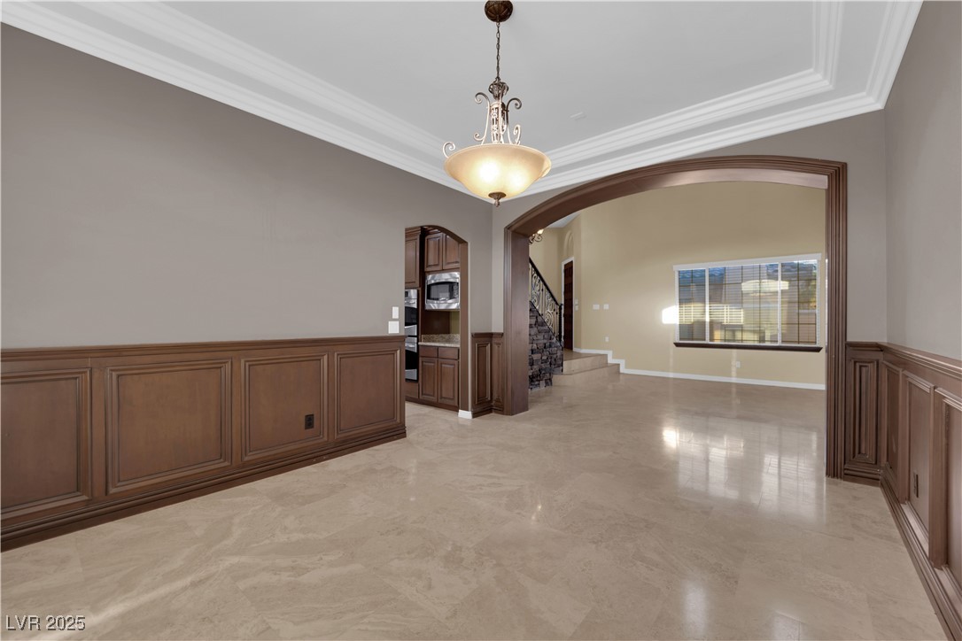 10057 Portula Valley Street Las Vegas, NV 89178 - Photo 10 of 56 Spare room featuring arched walkways, crown molding, a wainscoted wall, a decorative wall, and stairs