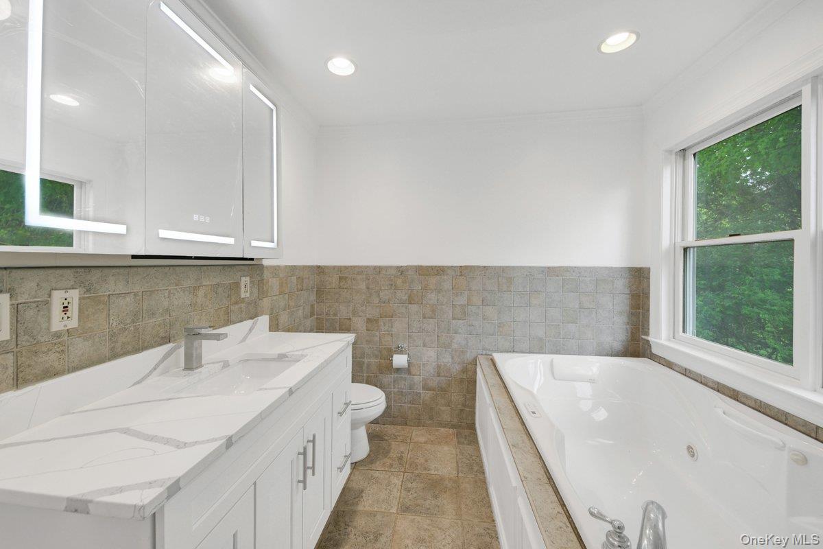 7 Rutledge Road Valhalla, NY 10595 - Photo 24 of 37 Bathroom featuring a dual-basin vanity with a quartz countertop and integrated sinks, built-in soaking tub, recessed lighting, and tile flooring