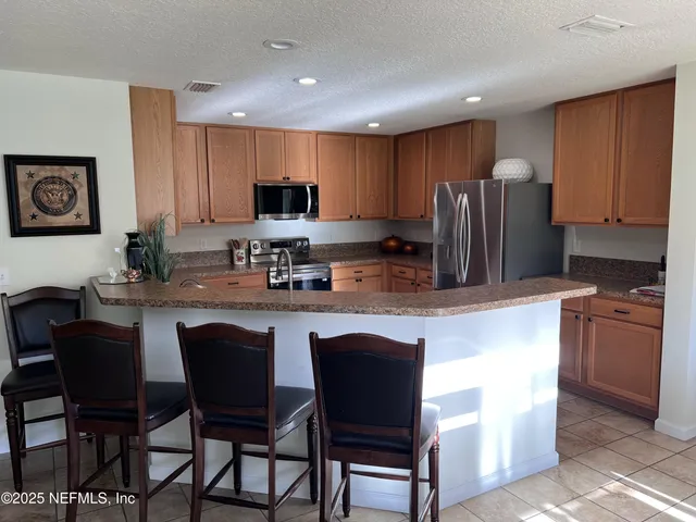 a kitchen with stainless steel appliances granite countertop a stove a sink a microwave a refrigerator and chairs