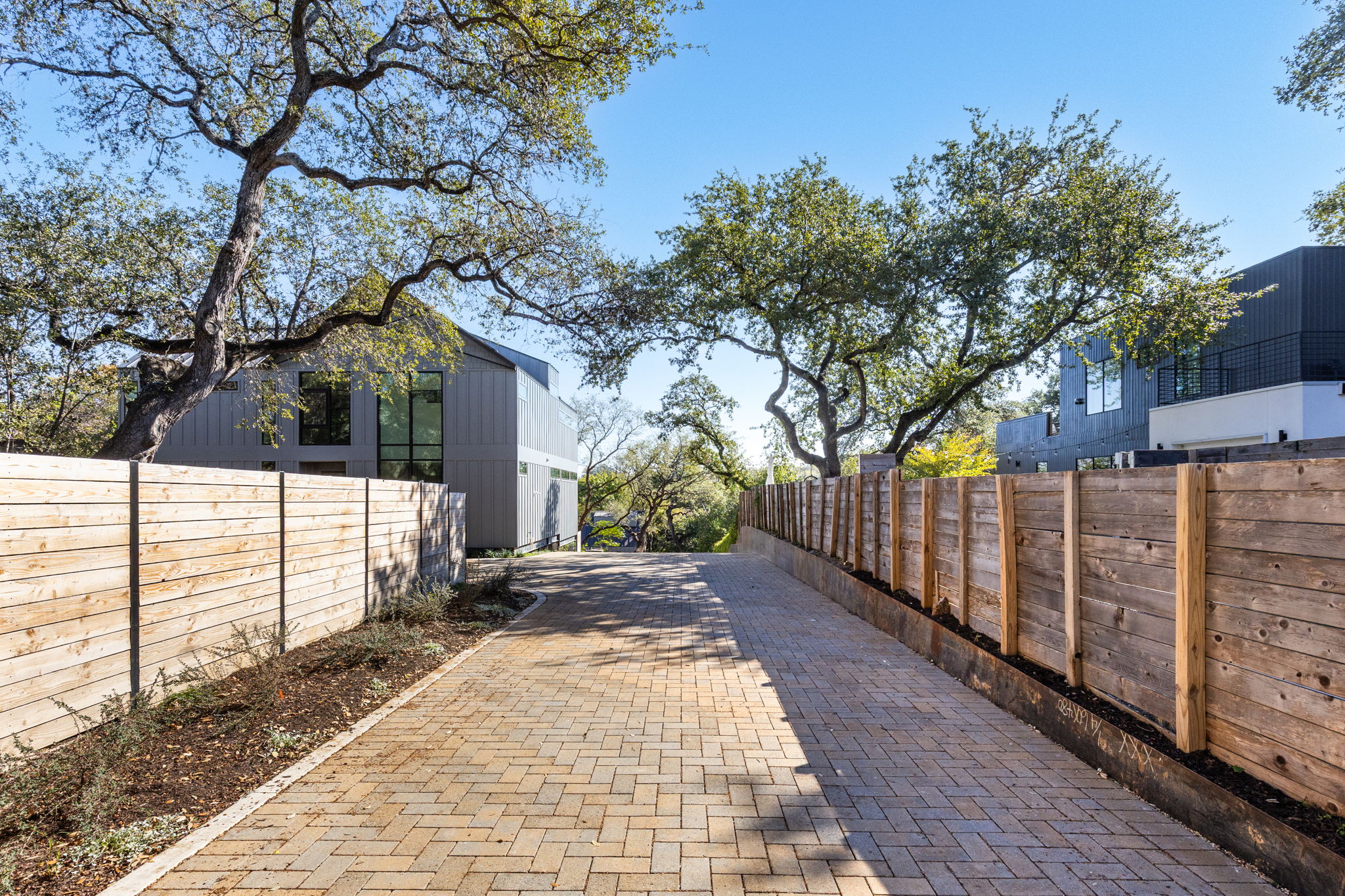 1603 Chelsea Lane, Unit 1 Austin, TX 78704 - Photo 5 of 34 An elegant paver driveway is bordered by horizontal wood fencing under a canopy of mature trees.
