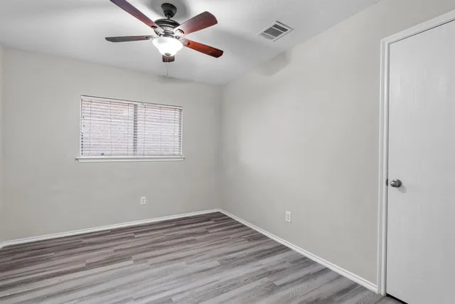 a view of an empty room with wooden floor and a ceiling fan