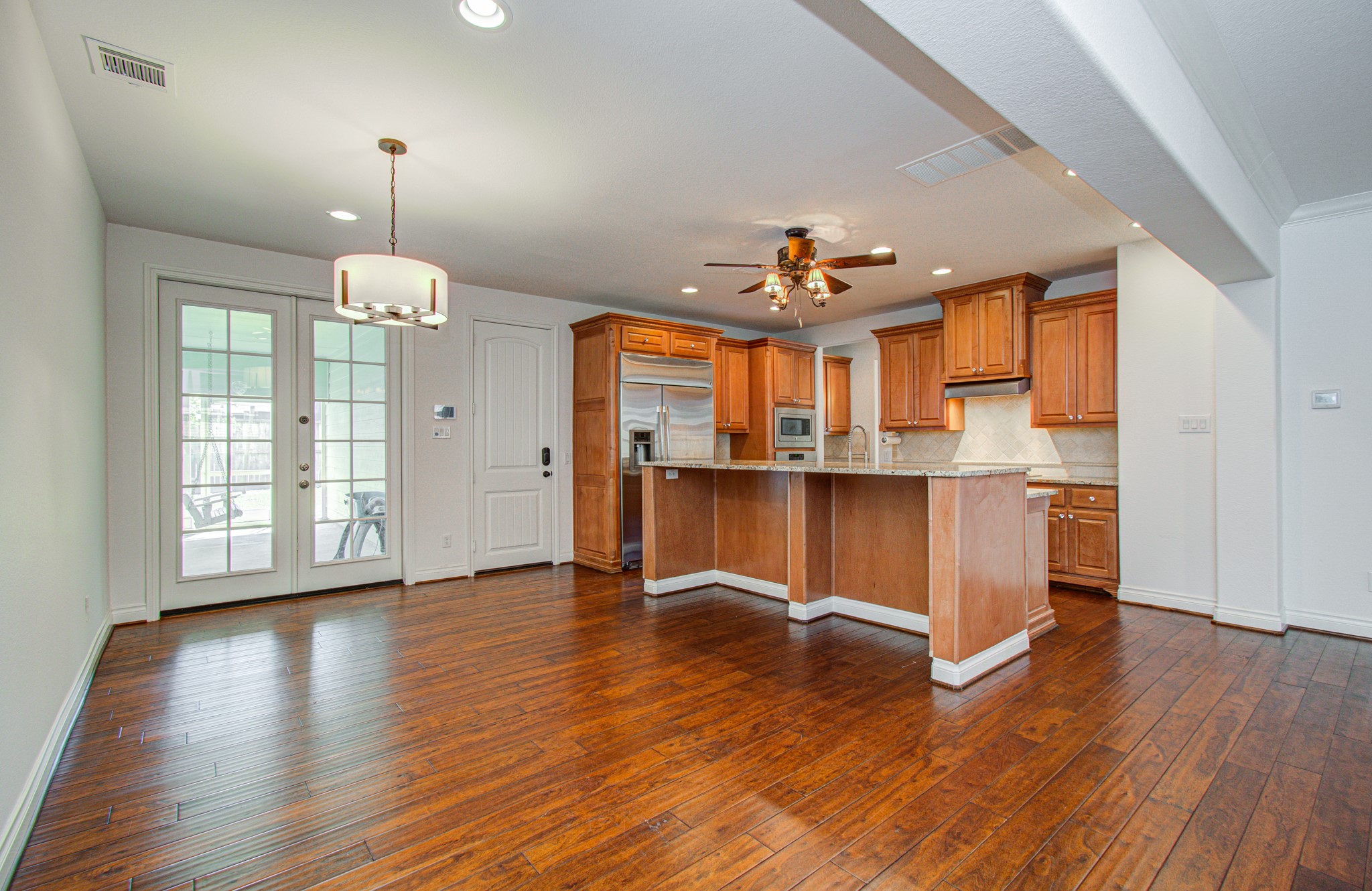 6621 North Main Street Houston, TX 77009 - Photo 10 of 41 This is a bright, open-concept kitchen and dining area with hardwood floors. It features a spacious kitchen with wooden cabinets, a large island, stainless steel appliances, and a ceiling fan. French doors lead to an outdoor space.