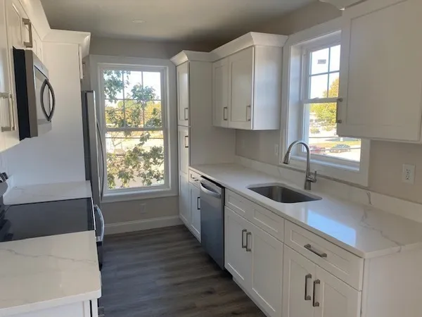 a kitchen with stainless steel appliances white cabinets a sink a window and a refrigerator