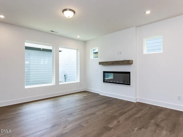 an empty room with wooden floor fireplace and windows