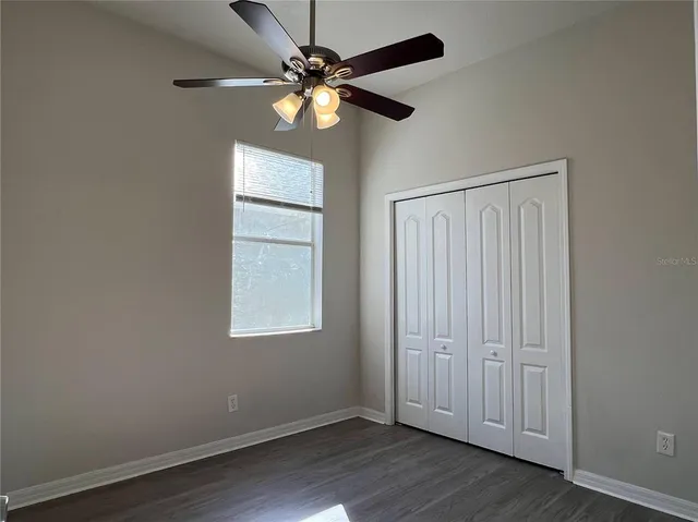 an empty room with wooden floor chandelier fan and windows
