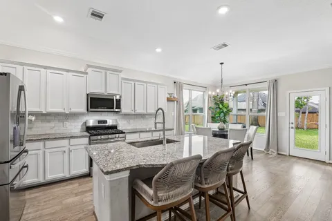 a kitchen with stainless steel appliances granite countertop a stove top oven a sink dishwasher a dining table and chairs with wooden floor