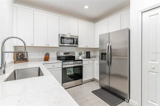a kitchen with stainless steel appliances granite countertop a refrigerator a stove a sink and white cabinets