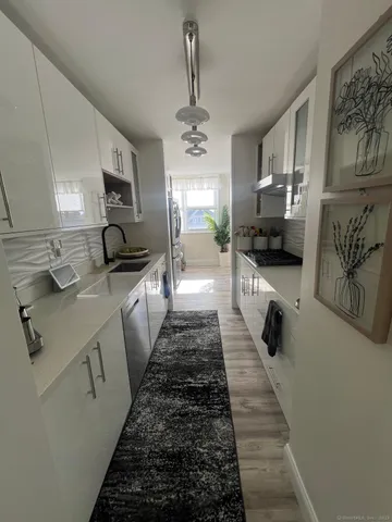 a large white kitchen with stainless steel appliances a stove a sink a refrigerator cabinets and wooden floor