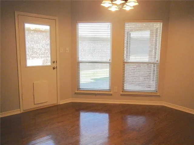 an empty room with kitchen view and wooden floor