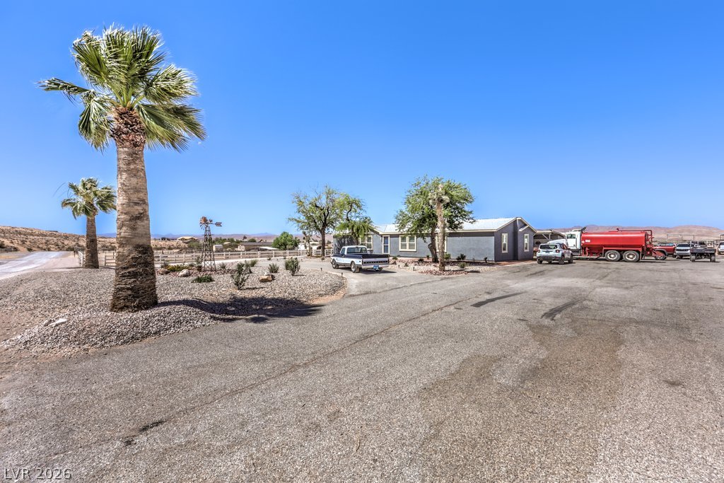 4375 Pinwheel Street Logandale, NV 89021 - Photo 2 of 52 Palm trees accent a sprawling rural property with a long driveway leading to a single-story home.
