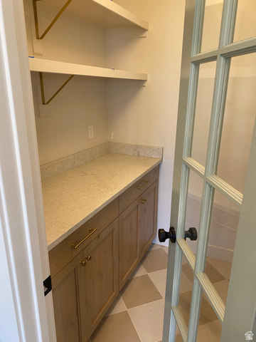4676 West 75 North, Unit 401 West Point, UT 84015 - Photo 21 of 25 Pantry featuring checkerboard floor tiles, built-in lower cabinetry with gold-tone hardware, a light-toned countertop, and open shelving with gold-tone brackets