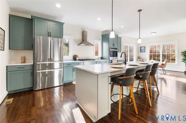 a kitchen with stainless steel appliances granite countertop a refrigerator a sink dishwasher a stove and a dining table with wooden floor