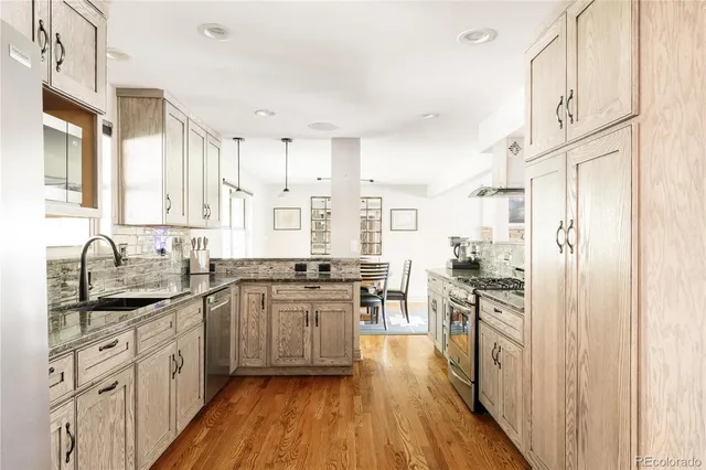 a kitchen with stainless steel appliances granite countertop a stove top oven a sink dishwasher a refrigerator and cabinets with wooden floor