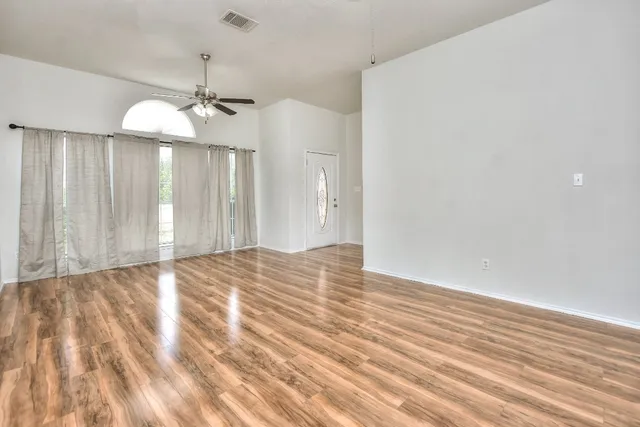 an empty room with wooden floor chandelier fan and kitchen view
