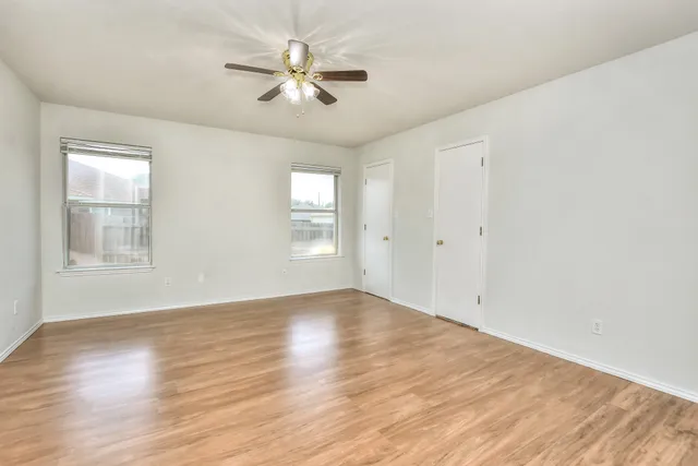 an empty room with wooden floor ceiling fan and windows