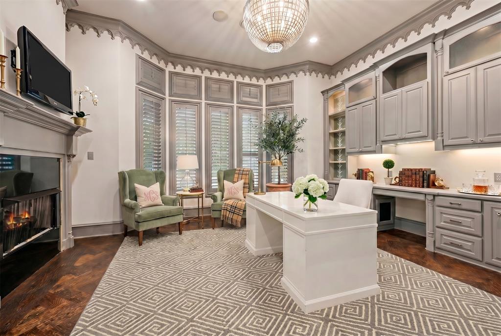 6900 Rockingham Court Colleyville, TX 76034 - Photo 13 of 40 Private office featuring a fireplace, custom built-in cabinetry with under-cabinet lighting, a chandelier, bay windows with plantation shutters, and patterned hardwood flooring. Ai staged.