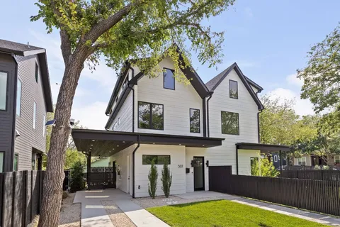 a view of a white house with a large tree and wooden fence