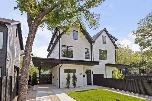 a view of a white house with a large tree and wooden fence