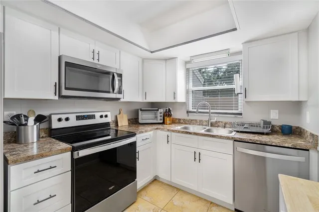 a kitchen with granite countertop white cabinets appliances a window and a sink