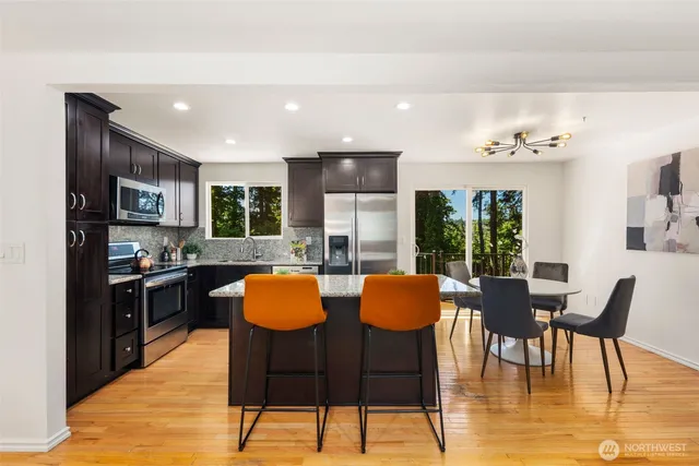 a kitchen with stainless steel appliances granite countertop a stove top oven a sink dishwasher a dining table and chairs with wooden floor