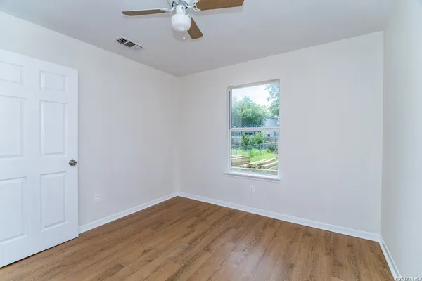 an empty room with wooden floor chandelier fan and windows