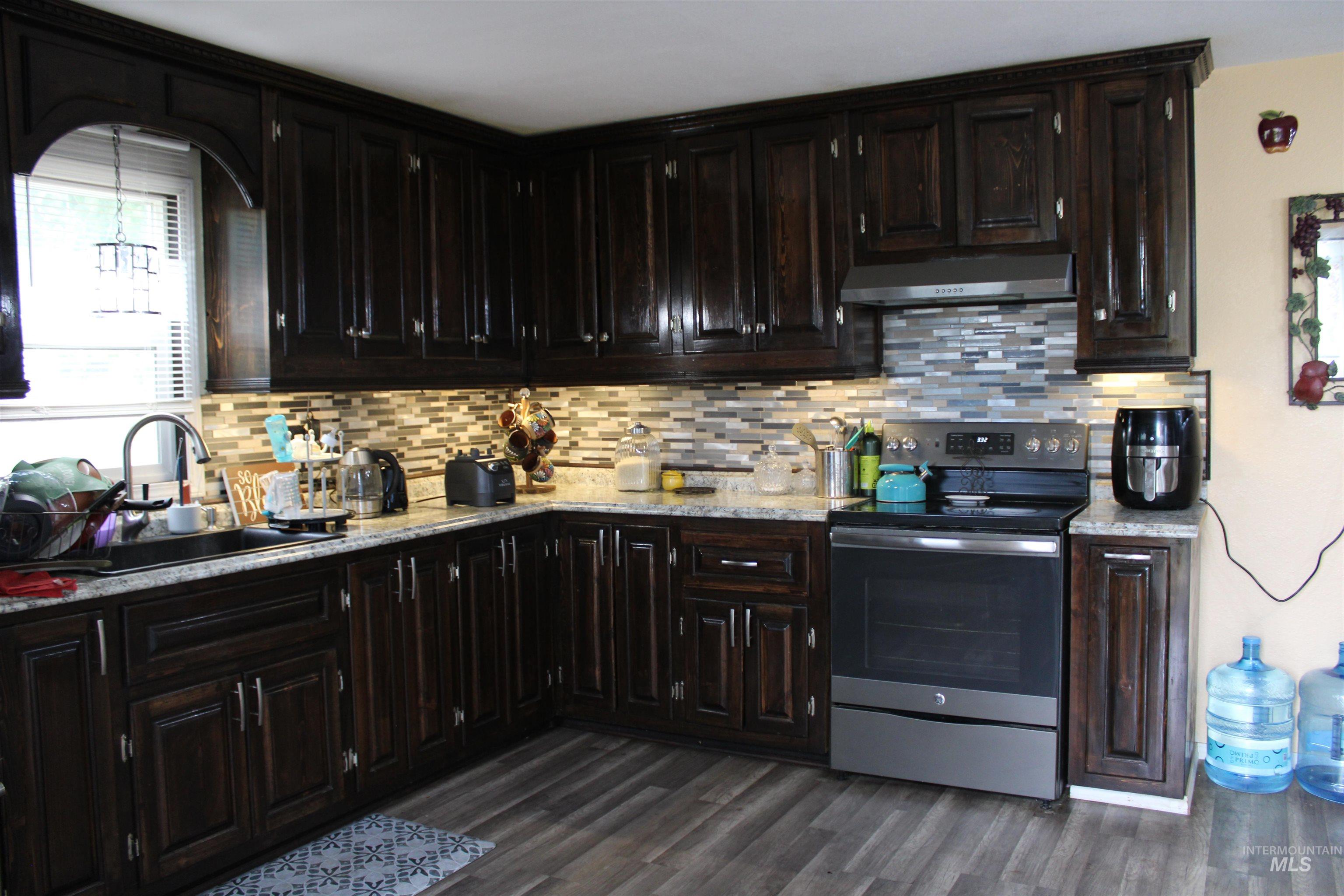 106 3rd Street West Declo, ID 83323 - Photo 5 of 23 Kitchen featuring electric range, tasteful backsplash, under cabinet range hood, dark wood finished floors, and light stone countertops