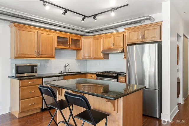 a kitchen with stainless steel appliances granite countertop a refrigerator a sink dishwasher a stove and white countertops with wooden floor