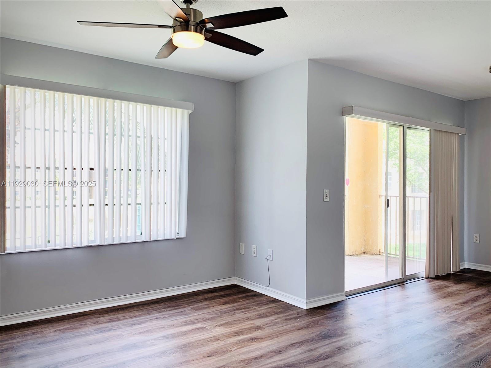 an empty room with wooden floor fan and windows