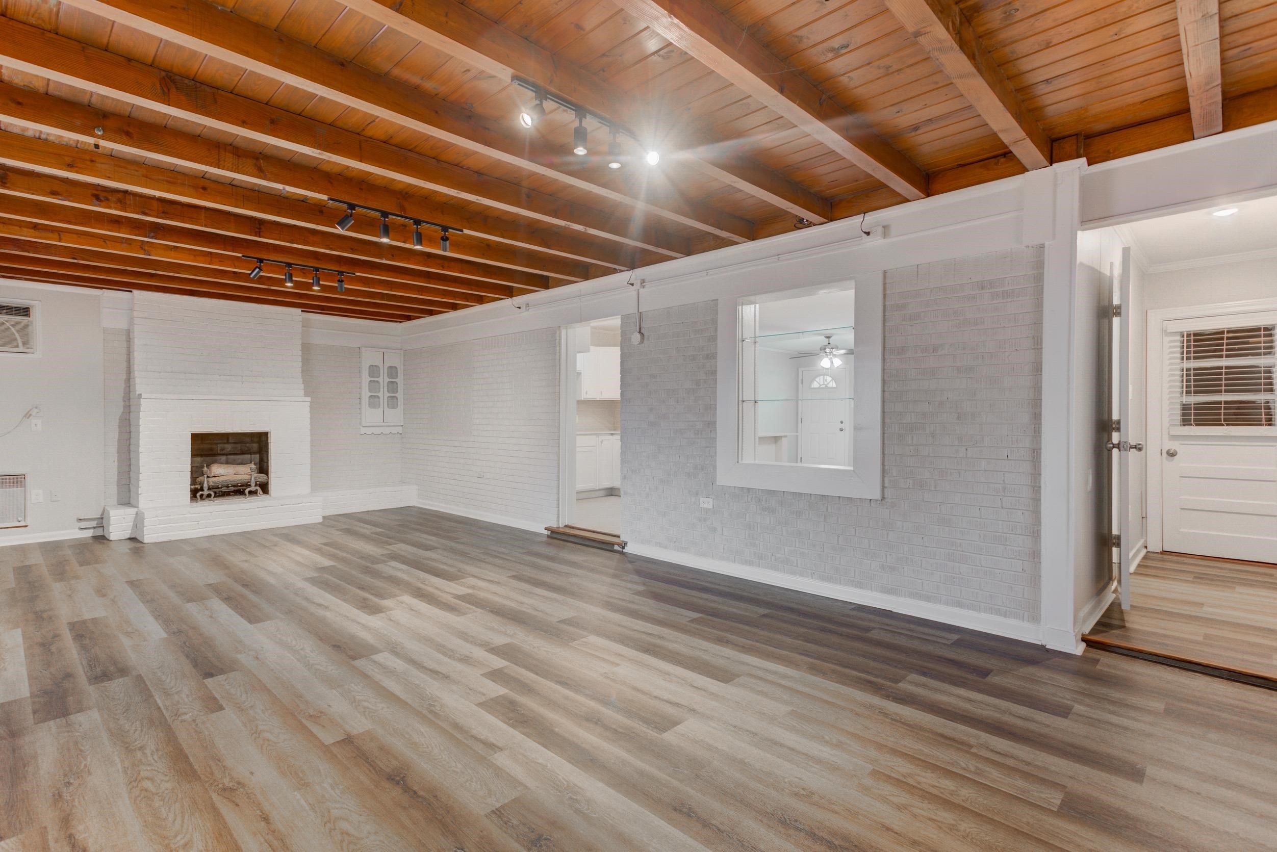1784 Sea Isle Road Memphis, TN 38117 - Photo 13 of 27 Unfurnished living room featuring a wooden ceiling with exposed beams, brick wall, track lighting, light wood-type flooring, and a fireplace