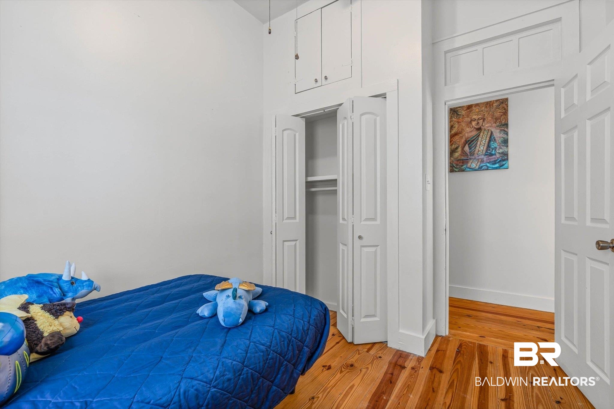 951 Montgomery Street Mobile, AL 36604 - Photo 18 of 22 Room featuring wood-finish flooring, white walls, a built-in closet with bi-fold doors, and an overhead storage cabinet