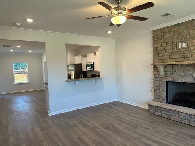 an empty room with wooden floor a ceiling fan a fireplace and windows