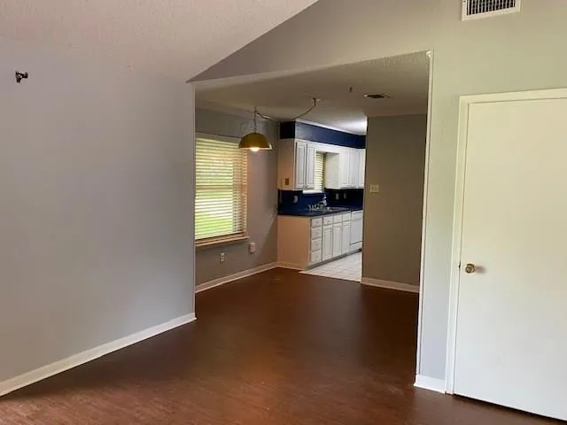 an empty room with wooden floor and a kitchen