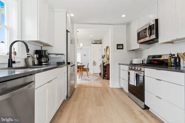 a kitchen with stainless steel appliances a stove top oven a sink a refrigerator and white cabinets with wooden floor