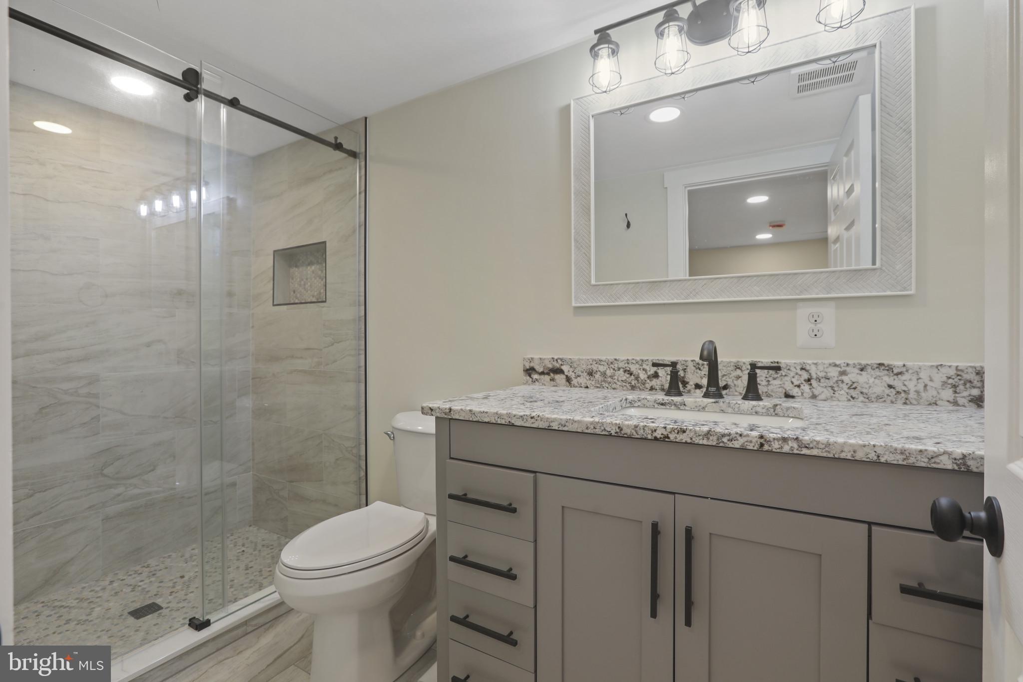 3828 10th Street Baltimore, MD 21225 - Photo 22 of 27 a bathroom with a granite countertop sink toilet a mirror a vanity and shower