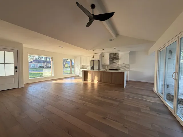 an empty room with wooden floor kitchen view and a window