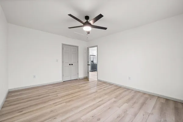 a view of an empty room with wooden floor and a ceiling fan