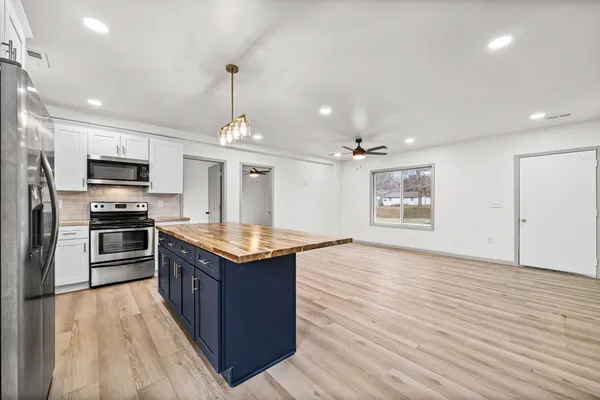 a kitchen with kitchen island granite countertop a stove top oven a sink dishwasher a refrigerator and a dining table with wooden floor